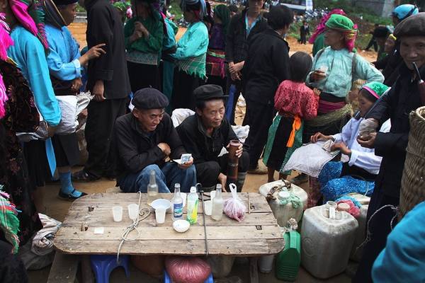 Hai người đàn ông dân tộc Mông ngồi hàn huyên, giữa những người người tấp nấp mua bán, đi lại trong chợ Đồng Văn buổi sớm.