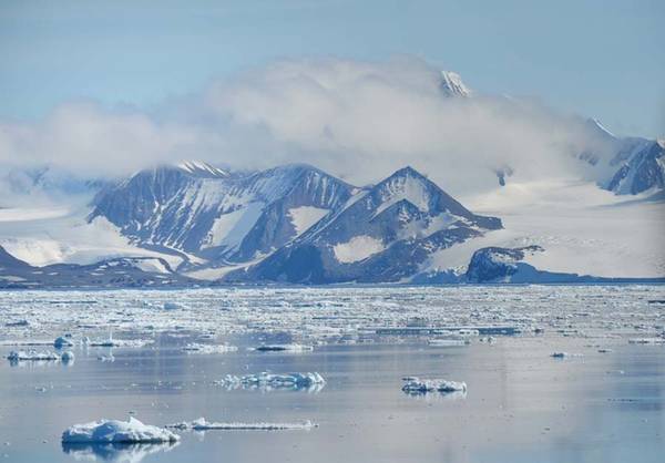 Những tảng băng nhỏ trôi nổi trên mặt biển Thái Bình Dương, trong khi các núi băng đá đằng xa hiện dần sau lớp mây trắng mờ.