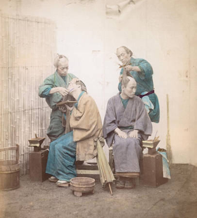 Hai người thợ cắt tóc cho khách. Cạo trọc trên đỉnh đầu rồi buộc lại là kiểu tóc đặc trưng của đàn ông Nhật Bản thời kỳ này. Ảnh chụp vào năm 1865.