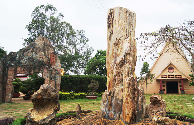 Thân gỗ hóa thạch lớn như chiếc linga đặt bên cạnh mái nhà rông, biểu tượng văn hóa Tây Nguyên tại Công viên Đồng Xanh, xã An Phú, thành phố Pleiku, tỉnh Gia Lai.