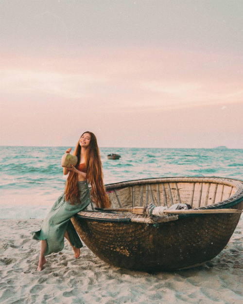 "Nàng công chúa" ngồi bên chiếc thuyền thúng, tự giới thiệu mình là một nàng "ngư dân" và thưởng thức một trái dừa địa phương ngọt lịm ở biển An Bàng (Hội An).