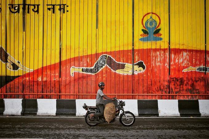 Người đàn ông này đang chở hàng hóa cồng kềnh đến nỗi không còn chỗ để chân trên chiếc xe máy nhỏ qua con đường vẽ graffiti màu sắc. Ấn Độ là thị trường xe máy hàng đầu thế giới, loại phương tiện này rất được ưa chuộng để di chuyển và chở đồ ở nơi đây.