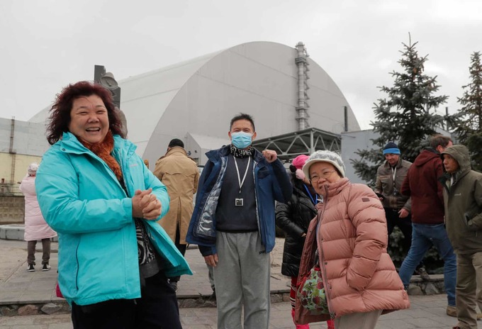 Du khách vui vẻ đứng trước công trình có mái vòm bao trùm phần còn lại của lò phản ứng số 4 thuộc nhà máy điện hạt nhân Chernobyl.  Một công ty làm tour tham quan Chernobyl cho biết số khách đặt tour tăng 40% sau khi series của HBO phát sóng giữa năm 2019. Một tour với hướng dẫn tiếng Anh tới đây có giá 100 USD một người.