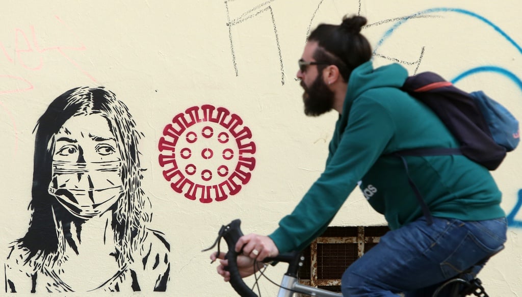 Hình ảnh con người đeo khẩu trang y tế để hạn chế sự xâm nhập của virus corona chủng mới thu hút người đi xe đạp. Bức tranh được vẽ trên một bức tường ở Berlin, Đức.
