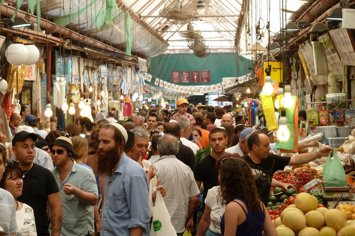 Hấp dẫn trong mắt khách du lịch  Du lịch đóng góp một phần lớn cho kinh tế. Đây là một trong những nguồn thu chính của thành phố, với ít nhất 3.5 triệu khách du lịch mỗi năm. Jerusalem thu hút khách bởi sự pha trộn của của truyền thống, tôn giáo, lịch sử, văn hóa và di sản hiện đại.   Khách du lịch cũng đổ về các khu ẩm thực để thưởng thức món sốt hummus (sốt đậu gà) trứ danh và các món ăn địa phương khác. Thậm chí, mỗi bước đi xuyên qua khu chợ cũng đủ khiến du khách phải trầm trồ. Chợ Mahane Yehuda là một khu vực nhộn nhịp với những nông sản tươi, cùng trang sức, quần áo và đồ trang trí. Ảnh: Wikimedia Commons/Deror avi.