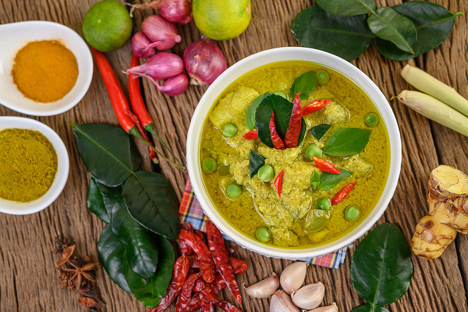 Green curry in a bowl and spices on wooden table.